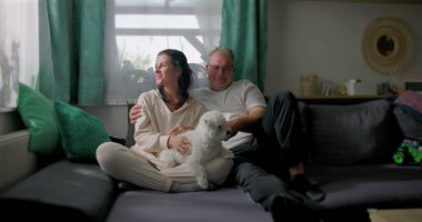 Çift evcil köpekle sıcak bir bağ paylaşıyor, evde samimi bir an yaratıyor, rahatlığın, aile dostluğunun ve birlikte huzurlu bir atmosferin tadını çıkarıyor.