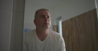 Adam aynada yüzünü inceliyor, yanak yanağa, tıraş olduktan sonra tenini kontrol ediyor, odaklanmış ifade, doğal ahşap banyo düzeneği, tımar ve kendine bakım rutini.