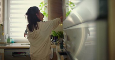 Anne ve bebek mutfakta etkileşime giriyor, çocuk sıcak aile rutininde tezgahı keşfediyor, sevgi ve şefkat sahnesinde.