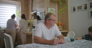 Baba yemek masasında küçük oğluyla etkileşime giriyor, aile zamanı mutfakta rahat bir sohbet ve bağlanma zamanı, arka plan modern mutfak kurulumu.