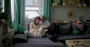 Çift evcil köpekle sıcak bir bağ paylaşıyor, evde samimi bir an yaratıyor, rahatlığın, aile dostluğunun ve birlikte huzurlu bir atmosferin tadını çıkarıyor.