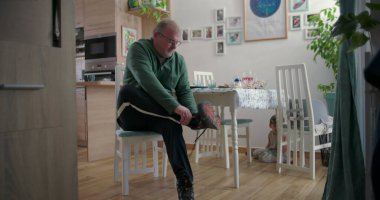 Babam sandalyede oturmuş çizmelerini bağlarken küçük bir çocuk da yemek masasının altından ahşap döşemeler ve dekorasyonlarla dolu sıcak bir aile yemek odasında gözetliyor.