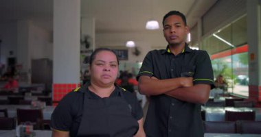 Latin çalışanlar, restoranın içinde el ele tutuşmuş vaziyette duruyorlar. Gün ortası vardiyaları arasında ciddi ifadeler sergiliyorlar.