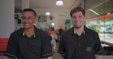 İki restoran garsonu yemek odasında birlikte gülüyor, yüzlerinin yan görünüşü birbirine doğru dönüyordu, iş günündeki sıradan bir an.