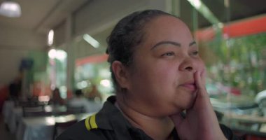 Latin bayan garson, restoranda yüz yüze duruyor. Düşünceli bir ifadeyle, iş vardiyası sırasında derin bir duraksamayla dışarı bakıyor.