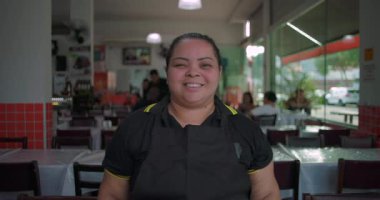 Latin lokantası çalışanı, yakın plan portrede gülümsüyor. Parlak yemek alanında sıcak ve dostane bir ifade.