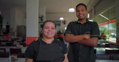 Latin çalışanlar restoran yemek alanında birlikte gülümsüyor. Şehir yemek servisinin gündüz vardiyasında keyifli bir mola sırasında üniformalarıyla ayakta duruyorlar.