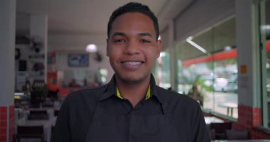 Latin lokantası çalışanı yemek alanında gülümseyen yakın plan portre, neşeli bir ifade ve kendine güvenen bir tavırla kapalı mekanda hoş karşılanıyor.
