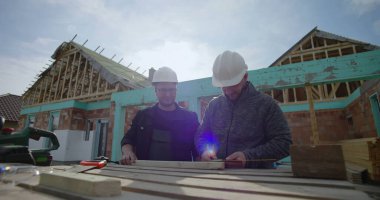 İnşaat sahasında ahşabı, takım çalışmasını işaretleyen ve detaylara, konut projesine, inşaat halindeki eve, çalışma maskesine, aletlere ve malzemelere odaklanan inşaatçılar