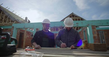 İnşaat sahasında ahşabı, takım çalışmasını işaretleyen ve detaylara, konut projesine, inşaat halindeki eve, çalışma maskesine, aletlere ve malzemelere odaklanan inşaatçılar