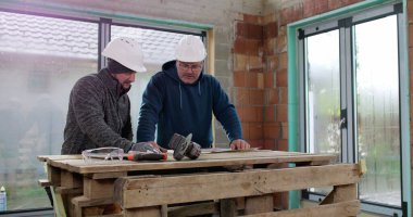 İnşaat ekibi inşaat başlıkları ve aletleri ile bir binanın içinde tadilat, takım çalışması, plan analizi ve çalışma planlarını tartışıyor.