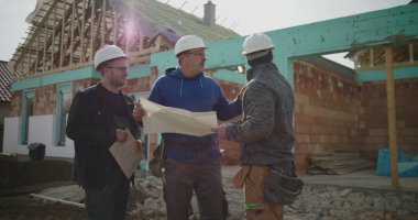 Bina planlarını inceleyen inşaat ekibi, inşaat planlarına odaklanmış tartışma, proje yönetiminde işbirliği, iş başında inşaat sektörü profesyonelleri