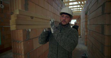 İnşaat işçisi inşaat halindeki evin koridorlarında kalaslar taşıyor ve devam eden inşaat projesinde odak ve güç gösteriyor.