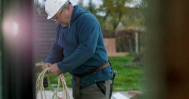 İnşaat sahasında miğferi olan işçilere kablo taşıyıp düzenlemek, el işçiliği ve dışarıda profesyonel aktiviteler sergilemek.
