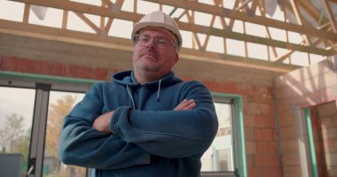 Kollarını kavuşturmuş, kasketli, kısmen inşa edilmiş bir binada duran kendine güvenen bir inşaat işçisi. İşinde profesyonelliği ve gururu somutlaştırıyor.