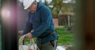 İnşaat sahasında miğferi olan işçilere kablo taşıyıp düzenlemek, el işçiliği ve dışarıda profesyonel aktiviteler sergilemek.