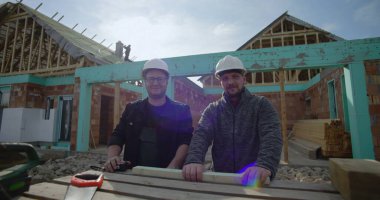 İnşaat alanında duran inşaatçılar, çerçeve altındaki ev, takım çalışması ve işbirliği, ahşap şapkalı iki adam, aletler ve malzemelerle çalışabilir, tamamlanmamış bir ev.