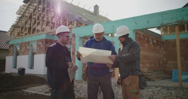 Bina planlarını inceleyen inşaat ekibi, inşaat planlarına odaklanmış tartışma, proje yönetiminde işbirliği, iş başında inşaat sektörü profesyonelleri