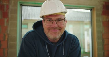 İnşaat alanında güler yüzlü, güvenlik kaskı takan, kendine güvenen, rahat ve pozitif çalışma ortamı sergileyen inşaat işçilerinin yakın çekimi.