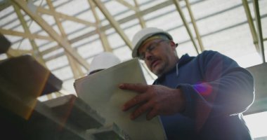 İnşaat denetçisi inşaat planlarını gözden geçirirken aynı zamanda inşaat çalışanı, takım çalışması ve yapısal proje rehberliği, güvenlik kaskları takılı