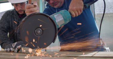 Açı öğütücü kullanan inşaat işçilerinin yakın çekimi, yoğun odaklanma, kıvılcımlar uçuşuyor, metal kesme, yenileme alanında güvenlik teçhizatı ile takım çalışması