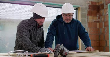 İnşaat ekibi inşaat başlıkları ve aletleri ile bir binanın içinde tadilat, takım çalışması, plan analizi ve çalışma planlarını tartışıyor.