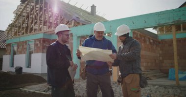 Bina planlarını inceleyen inşaat ekibi, inşaat planlarına odaklanmış tartışma, proje yönetiminde işbirliği, iş başında inşaat sektörü profesyonelleri