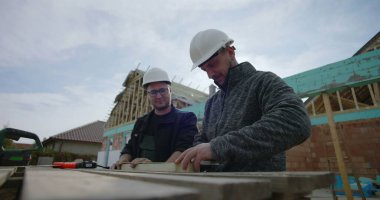 İnşaat alanındaki odunları ölçen müteahhitler, işbirliği çabası, hassas ölçümler, ev iskeleti, takım çalışması, konut projesi, başlıklar, görünür araçlar
