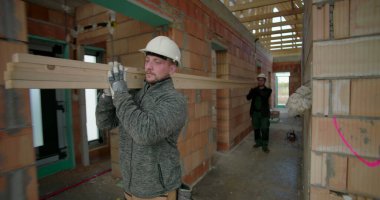 İnşaat işçisi inşaat halindeki evin koridorlarında kalaslar taşıyor ve devam eden inşaat projesinde odak ve güç gösteriyor.