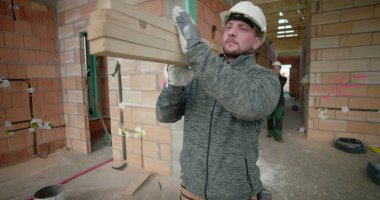 İnşaat işçisi inşaat halindeki evin koridorlarında kalaslar taşıyor ve devam eden inşaat projesinde odak ve güç gösteriyor.