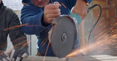 Açı öğütücü kullanan inşaat işçilerinin yakın çekimi, yoğun odaklanma, kıvılcımlar uçuşuyor, metal kesme, yenileme alanında güvenlik teçhizatı ile takım çalışması