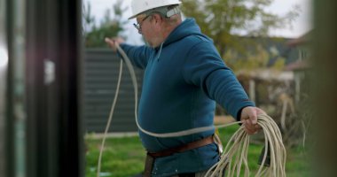 İnşaat sahasında miğferi olan işçilere kablo taşıyıp düzenlemek, el işçiliği ve dışarıda profesyonel aktiviteler sergilemek.