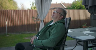 Dışarıda gözlüklü, derin derin bakan, bahçedeki yeşillik ve bahçeyle çevrili huzurlu anın tadını çıkaran bir adamın yakın çekimi.