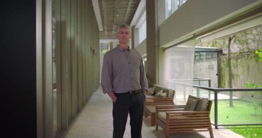 Orta yaşlı bir adam tüm vücut yapısında duruyor. Ofis koridorunun koridorunda hafifçe eğiliyor. Kendine güveni tam, mesleki davranışları rahat.