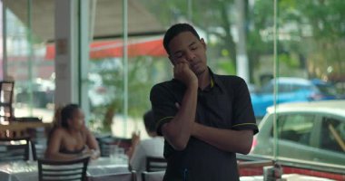 Yorgun, genç bir garson, kafasının üstünde restoranda dinleniyor, sessiz vardiya anında pencerenin yanında derin derin düşünüyor.