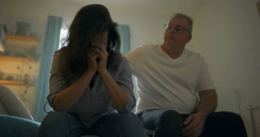 Yatakta oturan sıkıntılı eşi teselli etmek için eğilen koca, derin duygusal bağ, aşk temaları, destek, empati ve kişisel mücadelelerin üstesinden gelmek