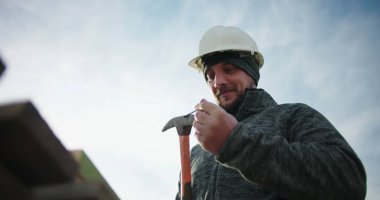 İnşaat işçisi çiviyi çekice çakıyor, tahtaya çakmaya hazırlanıyor, odaklanmış ve inşaat alanında marangozluğa hazır, konut inşaatında hassas ahşap işçiliği.