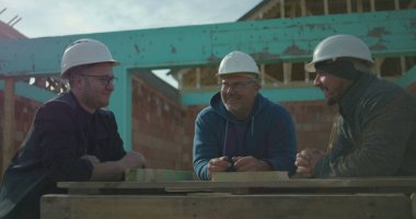 İnşaat işçileri inşaat alanında şakalar yapıyor ve birlikte gülüyorlar, iş arkadaşları arasında takım çalışması ve dostluk, inşaat halindeki konut yapısı, devam eden ev iskeleti