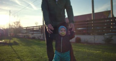 Babam, dışarıda çimenlerin üzerinde yürürken çömelmiş rehberlik ediyor. Bağlantı ve sevgiyi teşvik ediyor. Çocukluğun ilk adımları, arka bahçedeki aile ilişkileri.