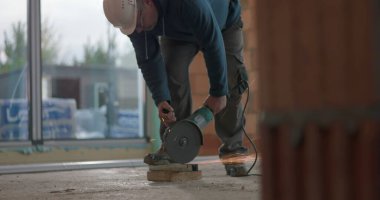 İnşaat işçisi çimento kesiyor, kıvılcımlar çıkarıyor, güvenlik kaskı yapıyor, göreve odaklanıyor, bina içi inşaata dikkat ederek ağır makineleri idare ediyor.