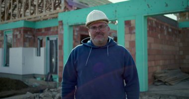 İnşaat işçisi inşaat alanında çalışıyor, devam eden projenin önünde profesyonel poz veriyor, şanlı inşaat işçisi iş yerinde çalışıyor, kararlılık ve gurur.