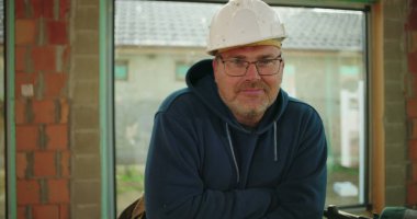 Çalışma tezgahının yanında poz veren inşaat işçisi, kısmen inşa edilmiş yapı, kendine güvenen ve ulaşılabilir ifade, inşaat alanı ortamı