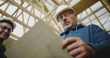 İnşaat işçileri inşaat başlıklarıyla mimari planlarını gözden geçiriyorlar, tamamlanmamış bir bina yapısının içindeki ayrıntılı planlara odaklanıyorlar, proje üzerinde çalışıyorlar.