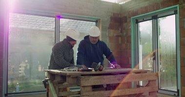 Tartışmalı inşaat işçileri, kapalı alandaki planları gözden geçirme, başlıklar, masadaki araçlar, işbirliği ve strateji, endüstriyel yapı projesi, takım çalışması