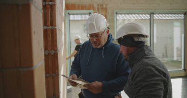 İnşaat işçisi tuğla duvarı ve mühendis gözlemi, inşaat sahasında açık duvarları ve geniş pencereleri olan takım çalışması