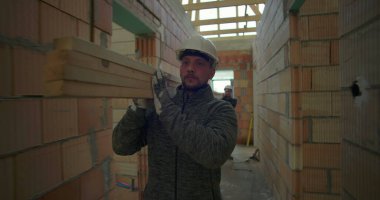 İnşaat işçisi inşaat halindeki evin koridorlarında kalaslar taşıyor ve devam eden inşaat projesinde odak ve güç gösteriyor.