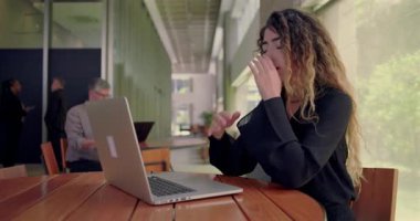 Tedirgin bir kadın dizüstü bilgisayara bakarken parmaklarıyla tapınakları tutuyor, zihinsel yorgunluk belirtileri gösteriyor ve ofis ortamında çalışmaktan yoruluyor.