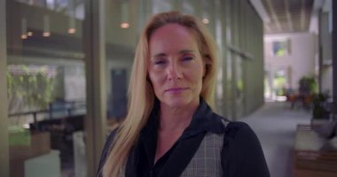 Modern koridorda kendine güvenen bir ifadeyle kameraya bakan bir kadın, azim ve profesyonelliği yansıtıyor.