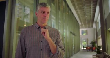 Orta yaşlı bir adam ofis koridorunda elleri ağızlarına yakın duruyor endişeli ifadeye bakıyor profesyonel ortamdaki endişe ve endişeleri iletiyor.