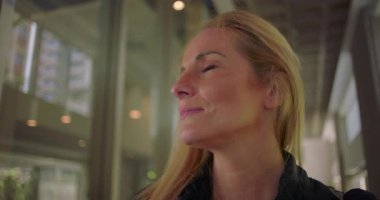 Modern binanın içindeki mesafeye özenle bakan kadına yakın dur. Odaklanma, kararlılık ve iç güveni sakin bir anda ifade et.